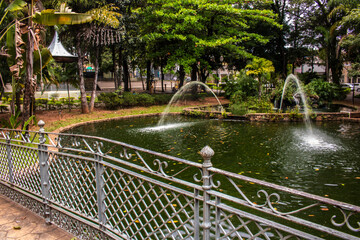 View of a classic metal bridge crossing a pond with fountains at a public garden in the city of Amparo, Sao Paulo state, Brazil.