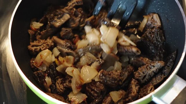 Frying sliced morels with onion in skillet. Closeup of stirring edible mushrooms with spatula during cooking process.