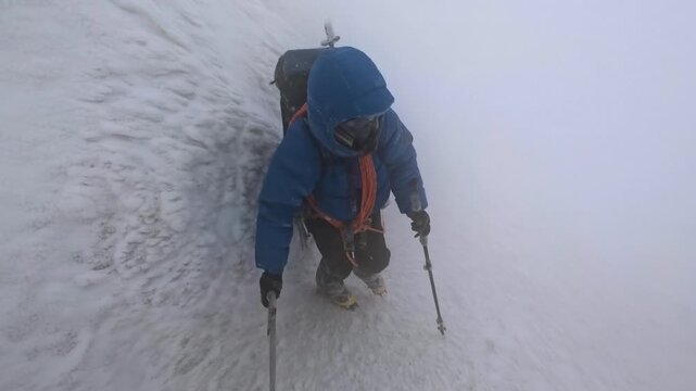 Climber with an ice axe and crampons battling a blizzard on a steep, snow covered mountain