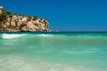 Obraz premium Turquoise sea wave near rocky coast under deep blue sky in Greece 