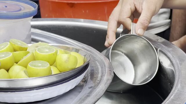 Street vendor pouring fresh water into a metal cup near sliced lemons for refreshing drinks
