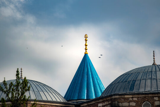Iconic green dome of mevlana and rumi tomb in Konya Turkey. Green Dome features turquoise tiles, Ottoman architecture and birds flying in a soft overcast sky. Evokes peace and spirituality.