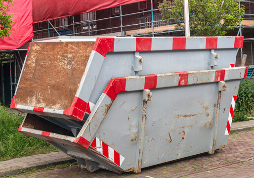 Two grey roll-off containers, stacked on top of each other, stand outside on the street in a residential area for renovation.