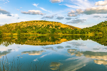 The massive granite dome of Enchanted Rock reflects perfectly on the calm, mirror-like surface of Moss Lake at sunset © ZL Visuals