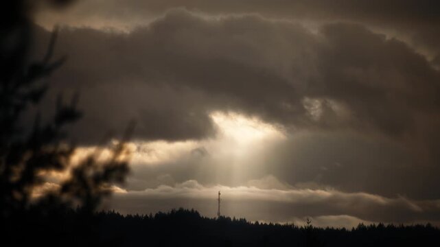 Sun ray breaking through golden sunrise clouds above trees silhouette