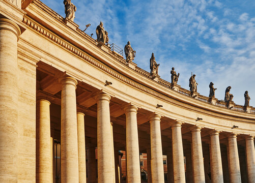 A section of Bernini's 17th-century colonnade at St. Peter's Square in Vatican City, featuring prominent Doric columns and statues of saints along the roofline, Rome, Italy, Europe 