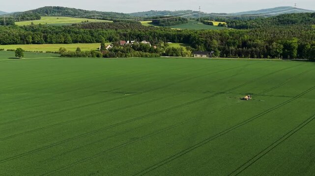 Aerial View of Tractor Working Green Field in Rural Hilly Landscape