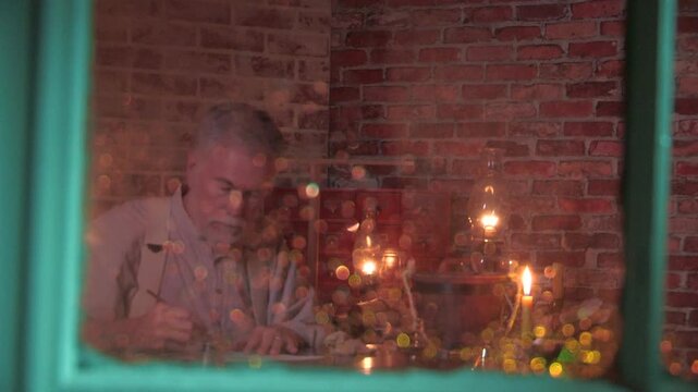 view through a rainy window of a man writing with a dip pen