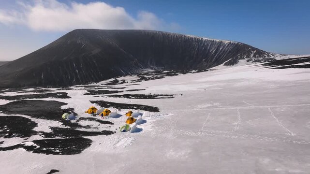 Aerial view of a base camp with yellow tents in a snow covered volcanic caldera on Deception Island