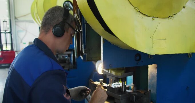 Blue collar factory worker controlling industrial press during metal part production. Manufacturing labor and workshop activity
