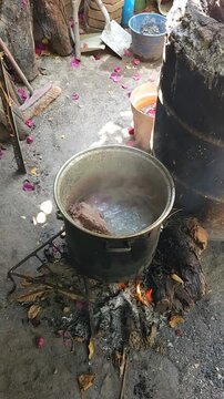 Pig head boiling in a traditional metal pot over an outdoor wood fire stove