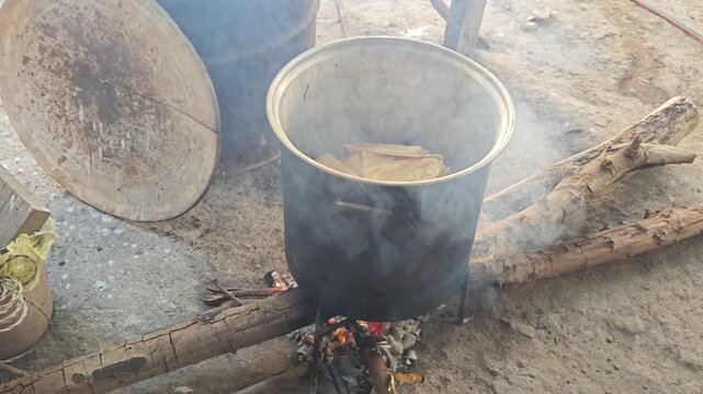 Steam and smoke rising from a large metal pot cooking traditional tamales over fire