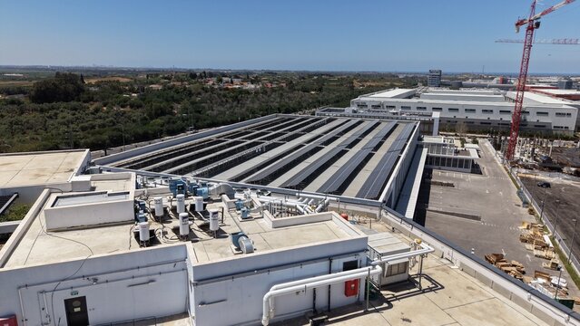 Aerial view of a large modern industrial facility with an extensive rooftop solar panel array, boilers, mechanical equipment and a crane


