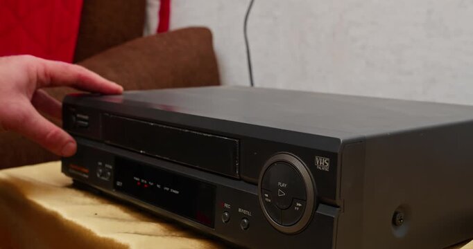 VHS tape being ejected from VCR slot, close-up detail. Retro media device and pre-digital video playback technology