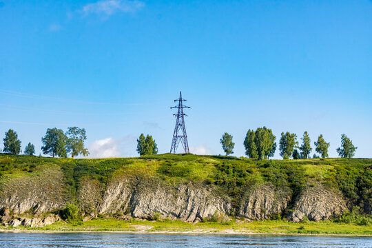High voltage transmission tower VL-35kV to VL-100kV standing on rocky riverbank with vertical sedimentary rock stratification