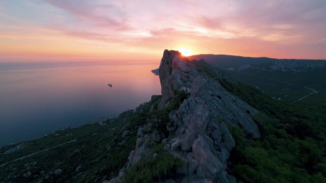 Flying over a mountain range against the background of the setting sun. The sea is visible below. High quality 4k footage FPV drone shoot