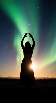 Woman Silhouetted with Arms Raised Under the Aurora Borealis.