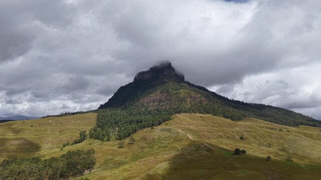 Dramatic view of Mount Lindsay peak under storm clouds with green forest and rolling hills in New South Wales, Australia