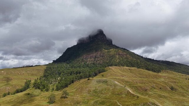 Dramatic view of Mount Lindsay peak under storm clouds with green forest and rolling hills in New South Wales, Australia