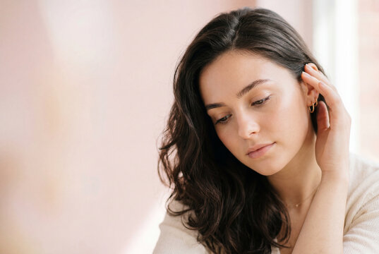 Pensive young woman touching face with glowing skin
