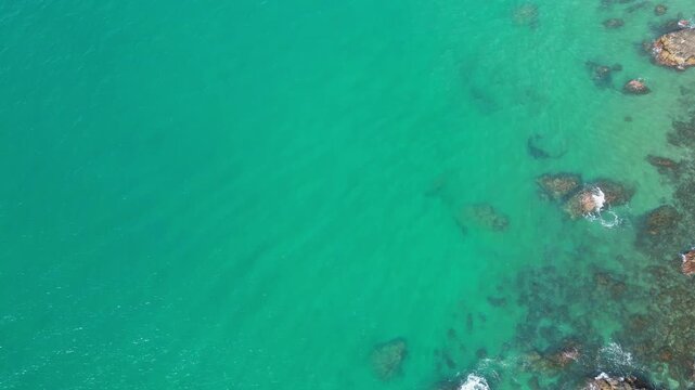 High angle bird's eye view of crystal clear turquoise ocean water with coral reefs and underwater rocks. Beautiful natural sea surface texture for summer travel or abstract background.