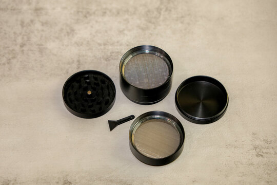 Herb Grinder Disassembled 4-Piece Aluminum Spice and Weed Grinder with Kief Catcher and Scraper Tool on Textured Background.