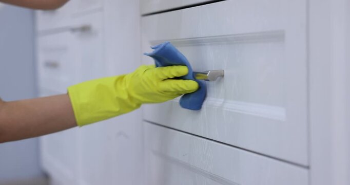 Spring cleaning. Woman in rubber gloves wiping metal knobs with rag at home, closeup. Camera moving down