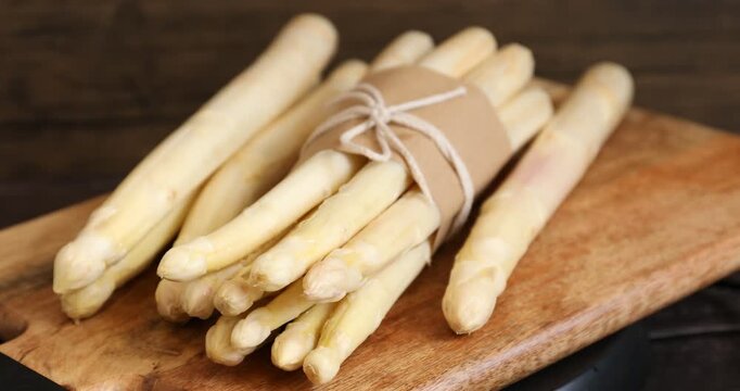 Woman putting raw white asparagus spears on black table, closeup