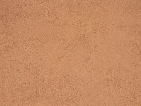 Texture and background of scraped pigmented mortar in salmon or earth tone. Granulated wall of colored cement, rough surface, Mediterranean style, exterior cladding, ornamental dividing zone.