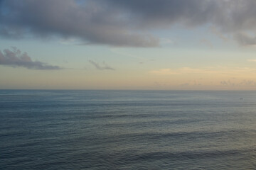 Fototapeta premium Peaceful open sea view stretching to a soft horizon under a cloudy, pastel sunset sky, providing a calm, minimalist ocean background perfect for text overlays and meditations. Uluwatu, Bali.