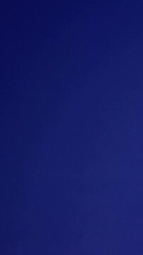 Vertical video: Shouting yellow tee woman waving green flag on blue backdrop, cheering, copy space
