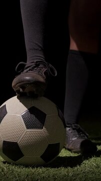 Vertical video: Shifting weight, legs in black socks pressing soccer ball on turf, prepping flick