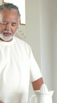 Vertical video: Partner reaching senior man in white T juicing fruit on juicer for juice in kitchen