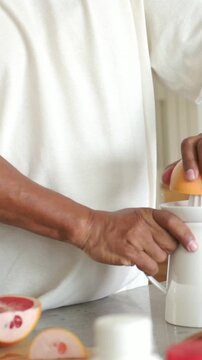 Vertical video: Reaching for citrus halves, man in white tee pressing juicer in kitchen for juice