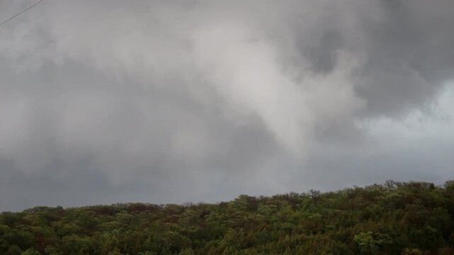 A funnel cloud spins in the sky over a forested ridge as the storm attempts to make a tornado.
