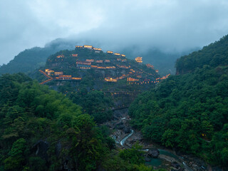 Fototapeta premium A view of the illuminated ancient buildings on the cliffs of Wangxian Valley in Jiangxi China during a misty evening