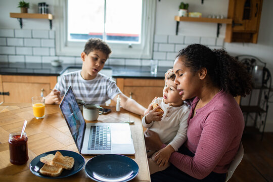 Mother multitasking with children during breakfast in home kitchen