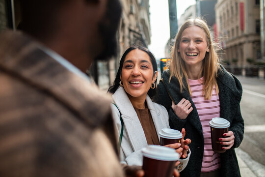Smiling friends with takeaway coffee on city street