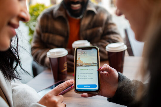 Friends booking a walking tour on a smartphone at a cafe