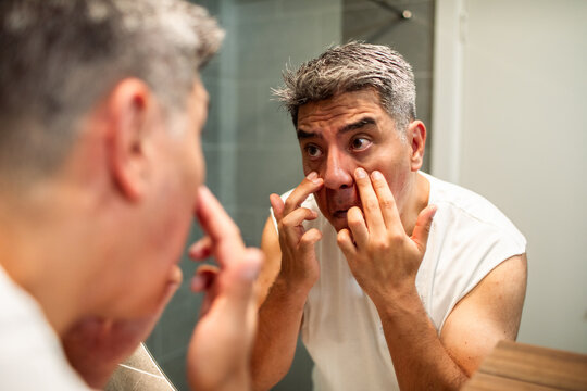 Middle-aged man examining under-eye bags in bathroom mirror