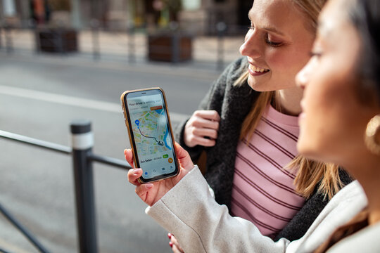 Two friends tracking rideshare arrival on smartphone on city street