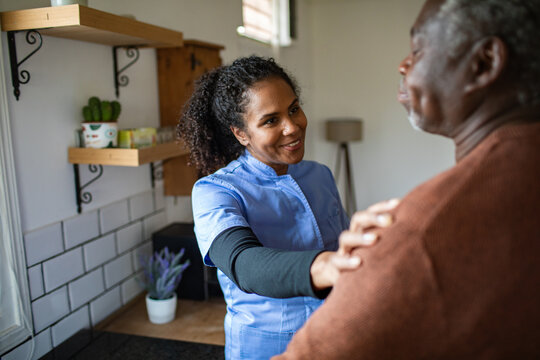Home caregiver comforting senior man in kitchen