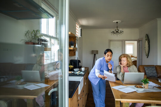 Home nurse assisting senior woman with paperwork in kitchen