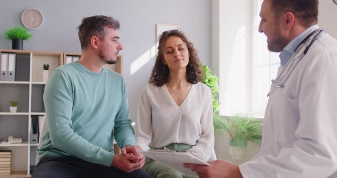 Male gynecologist doctor consults a happy family couple on pregnancy planning or ivf during a hospital visit. Consultation focuses on healthcare, medical advice, and family planning.