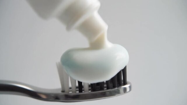 Squeezing fresh white and blue gel toothpaste onto a black toothbrush, illustrating the essential daily oral hygiene routine for dental health and a clean mouth