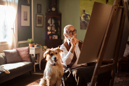 Senior artist painting on easel at home with dog