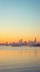 Naklejka premium A stunning golden hour view of the Melbourne city skyline reflected in the calm waters of Port Phillip Bay, with sailboats docked at the pier.