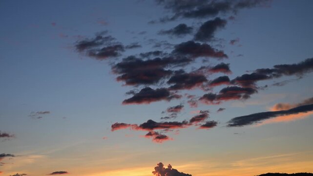 Breathtaking sunset sky with dark clouds moving slowly against a colorful orange and blue backdrop, creating a beautiful and dramatic evening or morning atmosphere