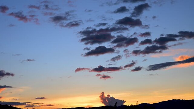 Dramatic clouds moving in a colorful sunset sky over a mountain silhouette, revealing a beautiful scenic twilight landscape with glowing orange and blue colors
