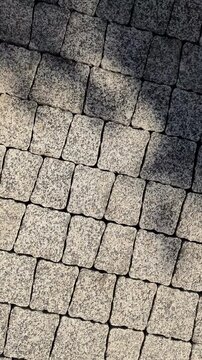 Vertical cinematic rotation of grey granite paving stones texture. Close up of cobblestone pavement pattern in bright sunlight with shifting tree shadows.